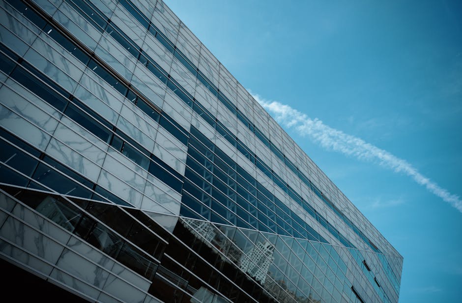 A striking low angle view of a modern glass building against a clear blue sky, emphasizing urban architecture